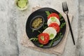 Caprese salad. Italian caprese salad with sliced tomatoes, mozzarella cheese, arugula, basil, olive oil in black plate over old Royalty Free Stock Photo