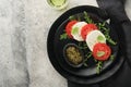 Caprese salad. Italian caprese salad with sliced tomatoes, mozzarella cheese, arugula, basil, olive oil in black plate over old Royalty Free Stock Photo