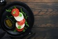 Caprese salad. Italian caprese salad with sliced tomatoes, mozzarella cheese, arugula, basil, olive oil in black plate over old wo Royalty Free Stock Photo