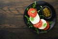 Caprese salad. Italian caprese salad with sliced tomatoes, mozzarella cheese, arugula, basil, olive oil in black plate over old wo Royalty Free Stock Photo