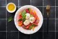 Caprese salad. Italian caprese salad with sliced tomatoes, mozzarella cheese, basil, olive oil in white plate over old brick tiles Royalty Free Stock Photo