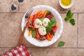 Caprese salad. Italian caprese salad with sliced tomatoes, mozzarella cheese, basil, olive oil in white plate over old brick tiles Royalty Free Stock Photo