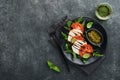 Caprese salad. Italian caprese salad with sliced tomatoes, mozzarella cheese, arugula, basil, olive oil in black plate over old br Royalty Free Stock Photo