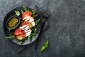 Caprese salad. Italian caprese salad with sliced tomatoes, mozzarella cheese, arugula, basil, olive oil in black plate over old Royalty Free Stock Photo