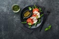 Caprese salad. Italian caprese salad with sliced tomatoes, mozzarella cheese, arugula, basil, olive oil in black plate over old Royalty Free Stock Photo