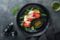 Caprese salad. Italian caprese salad with sliced tomatoes, mozzarella cheese, arugula, basil, olive oil in black plate over old Royalty Free Stock Photo