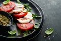 Caprese salad. Italian caprese salad with sliced tomatoes, mozzarella cheese, arugula, basil, olive oil in black plate over old Royalty Free Stock Photo