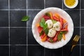 Caprese salad. Italian caprese salad with sliced tomatoes, mozzarella cheese, basil, olive oil in white plate over old brick tiles Royalty Free Stock Photo