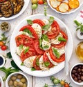 Caprese salad made of sliced fresh tomatoes, mozzarella cheese and basil served on a white plate on a wooden table. Royalty Free Stock Photo