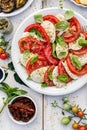 Caprese salad made of sliced fresh tomatoes, mozzarella cheese and basil served on a white plate on a wooden table. Royalty Free Stock Photo