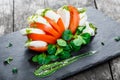 Caprese salad with Mozzarella cheese, tomatoes, pesto sauce and basil herb leaves on slate stone chalkboard on wooden background Royalty Free Stock Photo