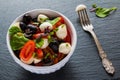 Caprese salad, small mozzarella cheese, fresh green leaves, black olives and cherry tomatoes in white vintage bowl on stone Royalty Free Stock Photo