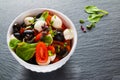 Caprese salad, small mozzarella cheese, fresh green leaves, black olives and cherry tomatoes in white vintage bowl on stone