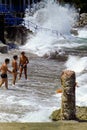 CAPRI, ITALY, JULY 1969 - Three boys defy the waves during a swell between the pebbles, the rocks and a Roman column on the beach. Royalty Free Stock Photo