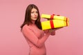 Capricious unhappy woman with brown hair in pink sweater disappointed with her birthday gift, holding unpacked present box in Royalty Free Stock Photo