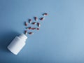 Capsules falling from the white bottle on blue paper background