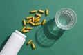 capsules are poured out from the white bottle without label, a glass of water on dark green background Royalty Free Stock Photo