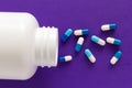 Capsules spilling out of white bottle. Purple background. Royalty Free Stock Photo