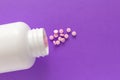 Capsules spilling out of white bottle. Violet background. Royalty Free Stock Photo