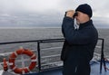 The captain of a cargo ship looks at the sea with binoculars.