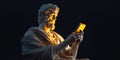 A marble statue of a philosopher holds a glowing phone. This artwork combines classical sculptures with modern Royalty Free Stock Photo