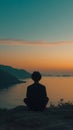 Person sitting peacefully on a hill overlooking the sea at sunset, with distant hills and a calm sea Royalty Free Stock Photo