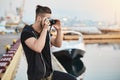 Capturing beautiful sunset. Dreamy creative european photographer in stylish outfit standing in harbour, taking picture