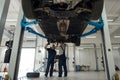 Car bottom raised on lift and mechanics working under Royalty Free Stock Photo