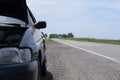 The car broke down on the road, a broken car with an open hood stands on an empty road