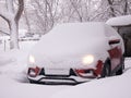 A car with burning headlights is buried under the snow after a snowstorm in a residential area Royalty Free Stock Photo