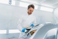 Car colorist man selecting color of automobile body element with paint matching samples.