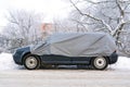 Car is covered with a car protective awning on a winter street