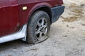 Car with deflated wheel on street. Old red car with deflated wheel parked on paved street in sunlight.