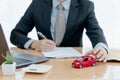 A car on desk envelope with man signing purchase documents in background. while hand complete the insurance policy, rental