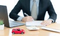 A car on desk envelope with man signing purchase documents in background. while hand complete the insurance policy, rental