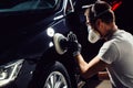 Car detailing - man with orbital polisher in auto repair shop. Selective focus.