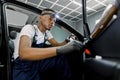 Car detailing and maintance. Portrait of young handsome African man worker in uniform and protective gloves performing