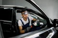 Car detailing and maintance. Young black male worker in professional uniform and gloves, applying special cream milk on