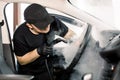 Car detailing, steam cleaning concept. Handsome man in black t-shirt and cap, worker of car wash center, cleaning car