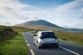 Car driving on empty scenic road trough nature by the lough inagh with mountains in the background