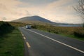 Car driving on empty scenic road trough nature by the lough inagh with mountains in the background