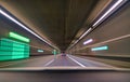 Car driving fast down interior tunnel, following another car.