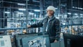 Car Factory: Confident Male Automotive Engineer Wearing Hard Hat, Standing and Monitoring Equipment Royalty Free Stock Photo