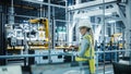 Car Factory: Female Automotive Engineer Wearing Hard Hat, Standing, Using Laptop. Monitoring Royalty Free Stock Photo