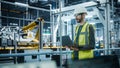 Car Factory: Male Automotive Engineer Wearing Hard Hat, Standing, Using Laptop. Monitoring, Control Royalty Free Stock Photo