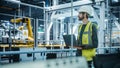 Car Factory: Male Automotive Engineer Wearing Hard Hat, Standing, Using Laptop. Monitoring, Control Royalty Free Stock Photo