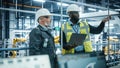 Car Factory: Project Manager and Automotive Engineer in Hard Hat, Talking, Using Laptop. Monitoring Royalty Free Stock Photo