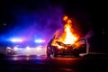 Car on fire at night with police lights in background