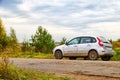 Car on a gravel dirt road next to green bushes and grass and under a sky with clouds. Natural road trip concept in autumn Royalty Free Stock Photo