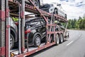 Car hauler big rig semi truck transporting cars on modular semi trailer running on the winding road